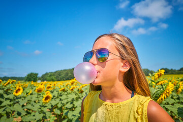Girl blowing bubble gum in sunflower field on sunny day