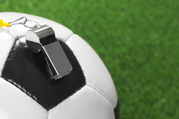 Football referee equipment. Soccer ball and metal whistle on green grass, closeup with space for...