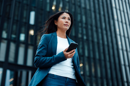 Businesswoman standing with smart phone in front of office building