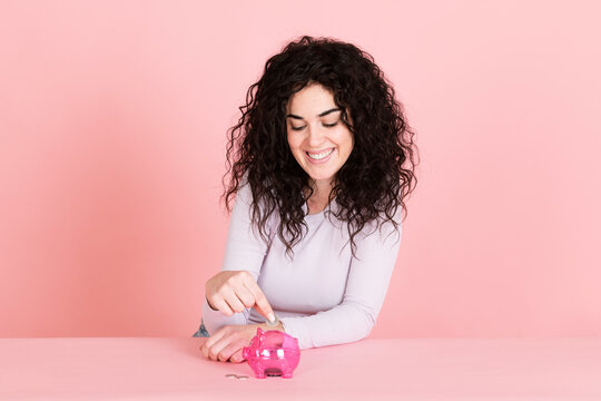 Happy woman saving money in piggy bank against pink background