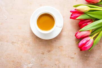Ein Tasse Kaffee mit Untertasse und pinke Tulpen auf einem braunen Tisch. Flat lay.