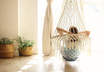 Woman relaxing in hanging chair at home