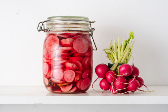 Jar with pickled radish near vegetables on shelf at home
