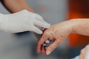 Close up of nurse insering IV cannula in vein, hand. Senior woman in intensive care unit in...