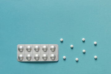 Medicine blister strip and three round white pills on a plain blue background. Pharmacy products....