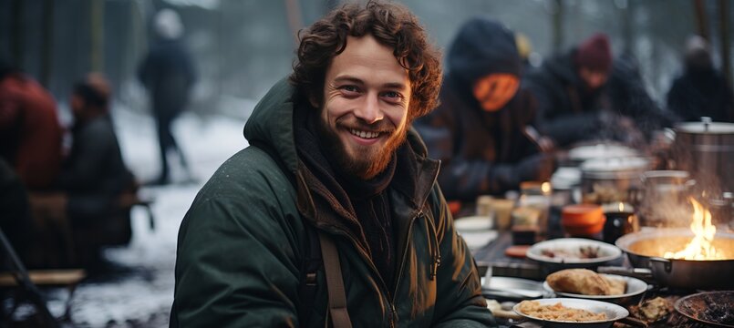 Young man cooking at winter tent camp in snow forest, survival and camping concept