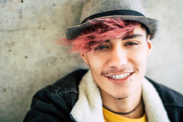 Portrait of young man with purple hair outdoors. Attractive, fashionable. Boy sitting on the ground with hat and modern hairstyle 18 year old teenager posing outside. - obrazy, fototapety, plakaty