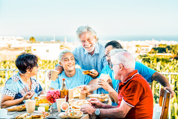 Multigenerational family having lunch on a terrace on a beautiful sunny day. 18 year old boy laughs with his grandparents celebrating. Lifestyle and family concept.​