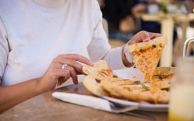 Close-up of woman sharing slice of delicious Italian pizza, sitting at table in a cozy outdoor...