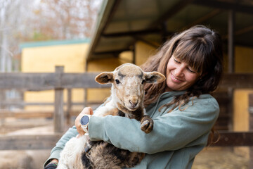 Happy young farmer woman hugging a baby sheep on a rural organic farm. Animal welfare and care in a...