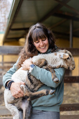 Happy young farmer woman hugging a baby sheep on a rural organic farm. Animal welfare and care in a barn.