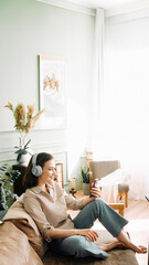 Joyful Connectivity. Young woman in wireless headphones, smiling as she engages in an online call on her smartphone