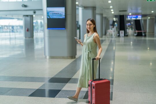 Asian woman with luggage using phone to check travel information at a transportation departure terminal