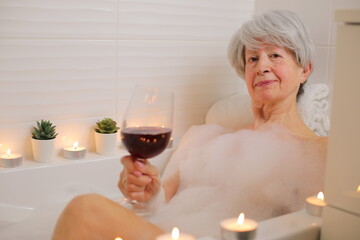 Senior woman drinking red wine in the bathtub  