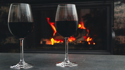 Two glasses of red wine on a background of a burning fireplace. Cozy atmosphere winter evening.