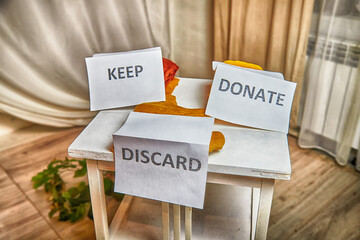 Signs with the words keep, donate, discard and fashion clothes folded in stacks in cozy room. The...