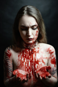 Portrait of young woman with red paint on her chest on dark background.