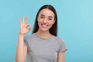 Young woman with clean teeth smiling and showing ok gesture on light blue background