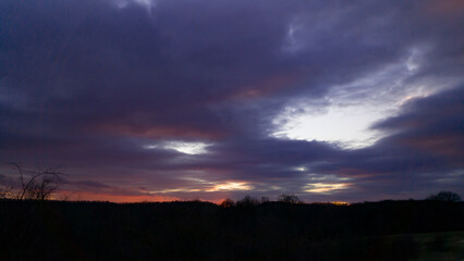 Vibrant sunset seen from the wild forest. Pastel colors in the evening sky. Cloud formations in abstract shapes