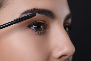 Naklejka premium Beautiful young woman applying mascara on black background, closeup