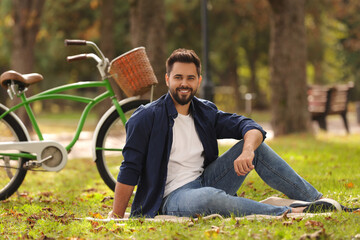 Young man sitting on green grass near bicycle in park