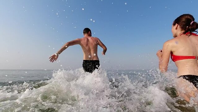 A man and woman run into the sea, kicking up the spray on the first day of their summer vacation. Slow motion. Water games. Vacation and recreation - Powered by Adobe