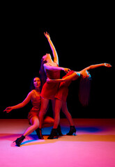 Passion and freedom of feelings. Three artistic young women in red dresses dancing against black background in neon light. Concept of modern dance style, creativity and beauty, art, hobby