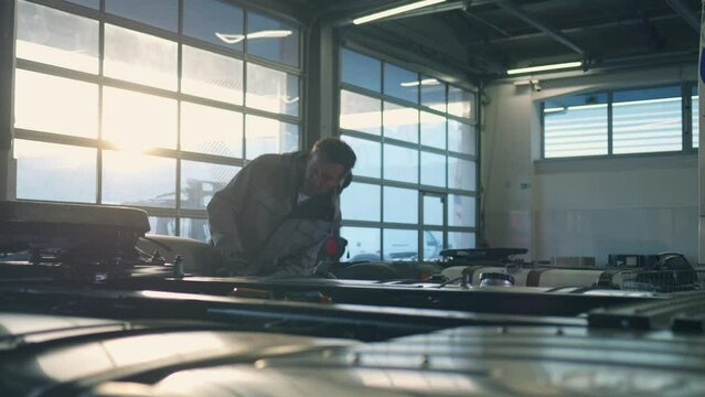 Auto mechanic examining lorry truck in sunlit repair station. Garage repairman inspecting trailer and walking in auto service shop medium tracking shot