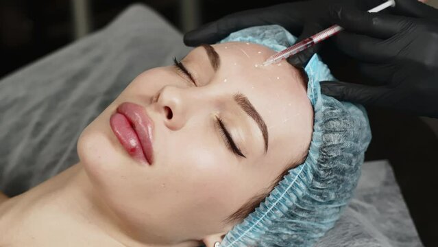 Face woman getting beauty injection in cosmetic clinic. Close up cosmetologist doing botox injection in forehead to patient in beauty clinic. Rejuvenation, injectable cosmetology and medicine concept