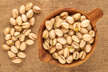 Small amount of roasted pistachios with wooden cup on jute cloth, macro, top view.