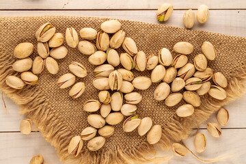 Small amount of delicious pistachios with jute napkin on wooden table, macro, top view.