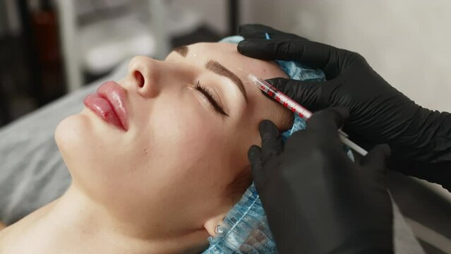Face woman getting beauty injection in cosmetic clinic. Close up cosmetologist doing botox injection in forehead to patient in beauty clinic. Rejuvenation, injectable cosmetology and medicine concept
