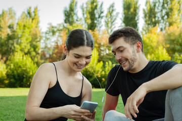 Chica compartiendo música con un chico en su móvil. Pareja escuchando música en un parque....