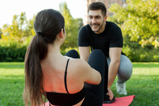 Entrenador personal sujetando a chica haciendo abdominales en un parque. Gente joven. Estilo de vida saludable.