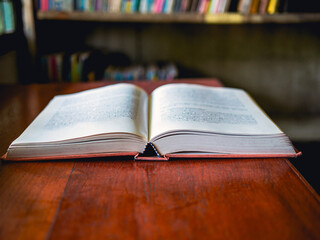 An open book or textbook vintage style on wooden table in the library and the bookshelves background.Education learning concept