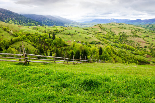 carpathian countryside in spring. wooden fence on the grassy hill. mountainous rural landscape of ukraine on a cloudy day