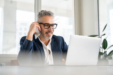 A mature businessman casually talks on the phone, his demeanor relaxed yet professional within a modern office space. This image captures the essence of contemporary corporate communication