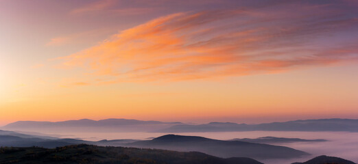 panorama of a sky above the carpathian mountain range with fog in the valley at dawn. clouds in red and orange colors of a rising sun