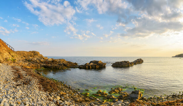 pebble sea shore of bulgaria with rocks at sunrise. beautiful outdoor scenery with view in to the horizon beneath a clouds on the blue sky. summer leisure and relax background