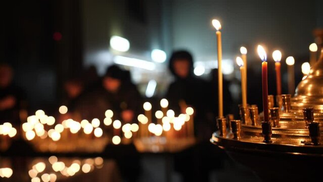 Lit candles on a holder, people in prayer in the background