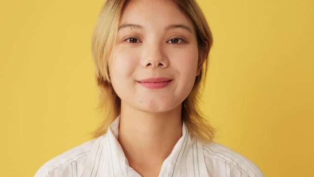 Close-up, woman opens eyes and looks at camera with smile isolated on yellow background in studio
