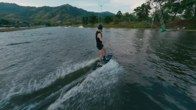 Profi wakeboarder man riding board jibbing slide ramp extreme trick aerial view. FPV sport drone close shot male enjoy wakeboarding speed race water splash ride activity tropical
