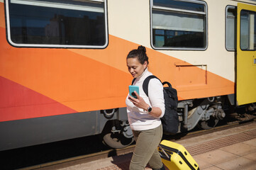 Female commuter harrying up to board train, checking her mobile phone while walking along the...