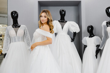 Pretty young woman is choosing a wedding dress in the shop. The bride-to-be is wearing a wedding dress for fitting