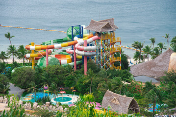 Close-up beach side water park colorful slides ride tropical themed family aquapark lush green...