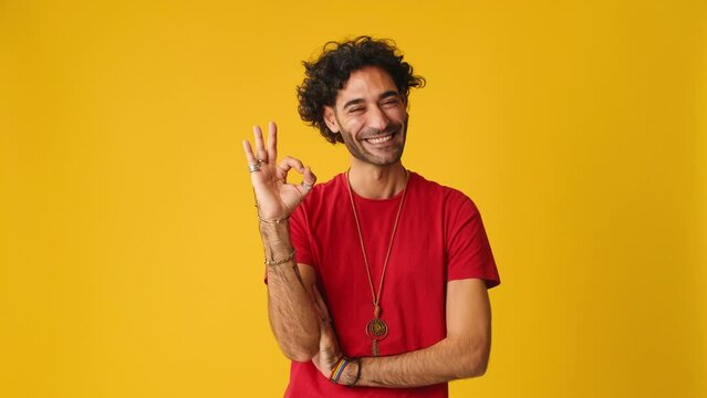Happy man showing ok gesture looking at camera isolated on yellow background in studio