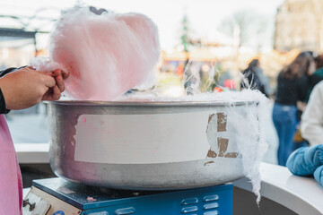 A cropped unrecognizable person making a large fluffy cotton candy at a funfair with a spinning machine