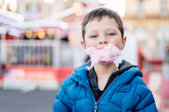Happy boy looking at camera with cotton candy stuck to his face enjoys a fun day at the funfair