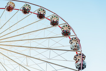 From below static Ferris wheel against a clear blue sky, showcasing its symmetry and colorful patterns on the passenger cabins
