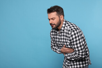 Unhappy man suffering from stomach pain on light blue background, space for text